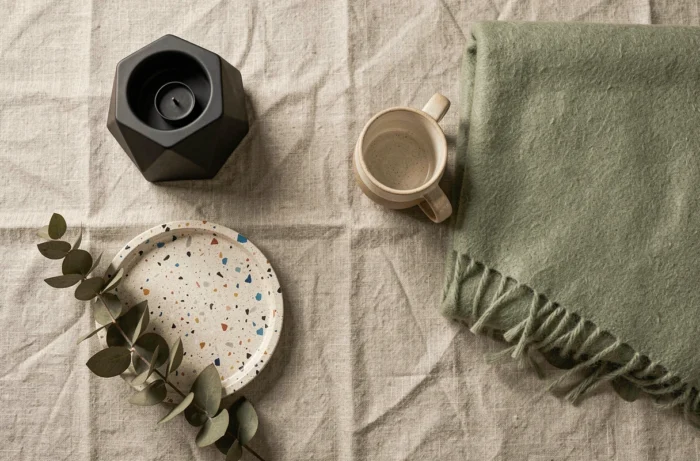 Flat-lay d'accessoires décoratifs tendance sur fond de lin : bougeoir géométrique, plateau en terrazzo, mug en céramique et laine douce